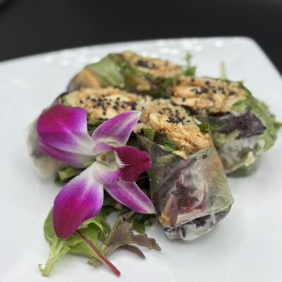 Close up image of a chicken teriyaki summer rolls garnished with an orchid flower