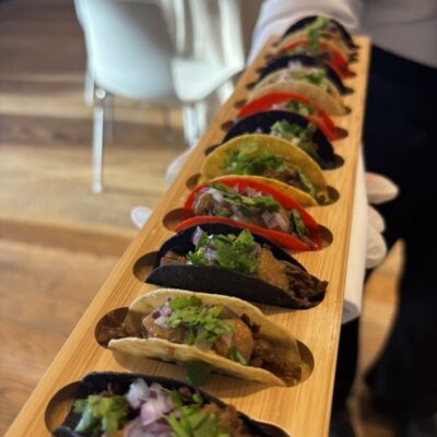 Server holding wood board filled with mini tacos