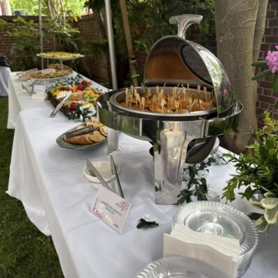 Buffet of cheese, mini burgers on more on white tablecloths in a garden setting