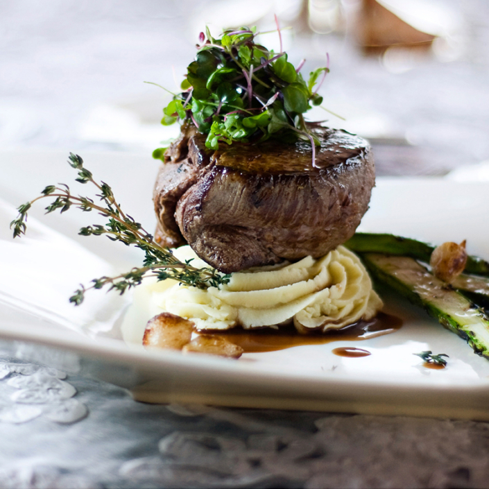 Beef Tenderloin atop piped mashed potatoes with microgreens on top.